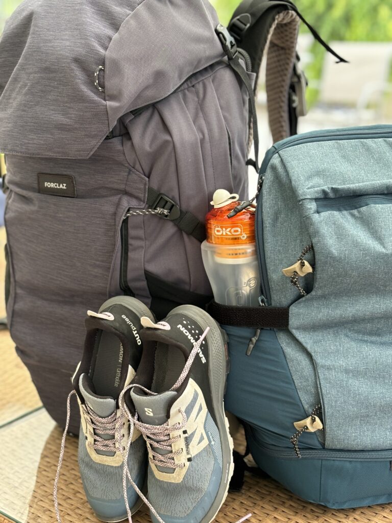 Sacs à dos et paire de baskets posés au sol, prêts pour le voyage.