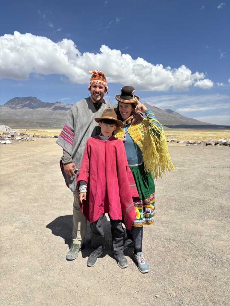 Famille en voyage vêtue de costumes traditionnels andins dans un paysage de montagne, ciel bleu et nuages blancs.