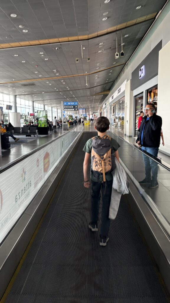 Jeune garçon de dos marchant à l’aéroport, prêt à vivre l’aventure du voyage.