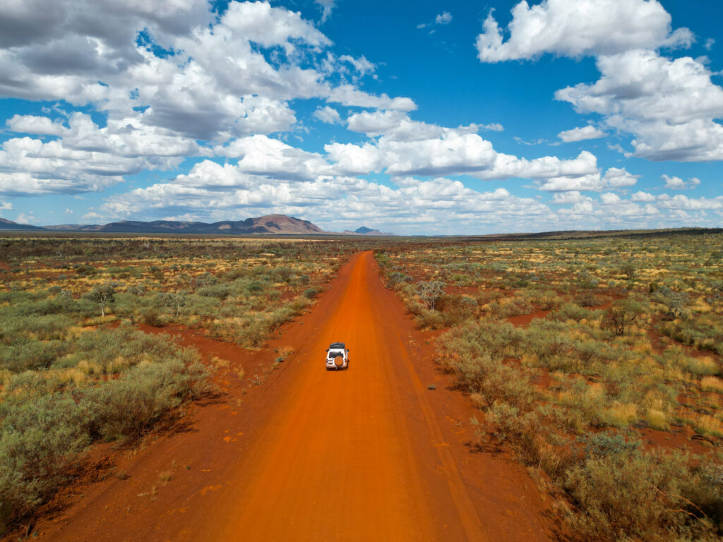 Vue aérienne par drone d’un 4x4 roulant sur une piste de terre rouge en Australie, avec Amaya et Maxime à bord.