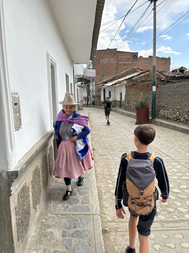 Un enfant voyageur marche dans une rue pavée et croise une femme en habits traditionnels péruviens.