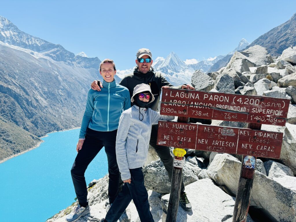 Une famille française souriante devant le panneau d’altitude au Lac Parón (4 300 m), avec la chaîne enneigée en arrière-plan.