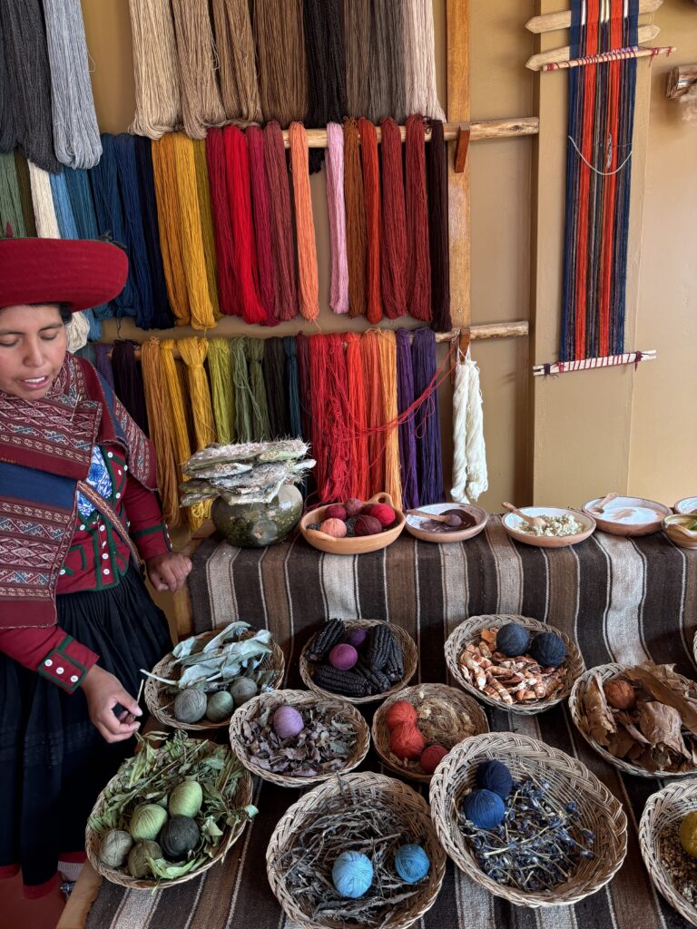 Femme péruvienne en habit traditionnel présentant des laines colorées teintées naturellement avec des plantes et matières premières.