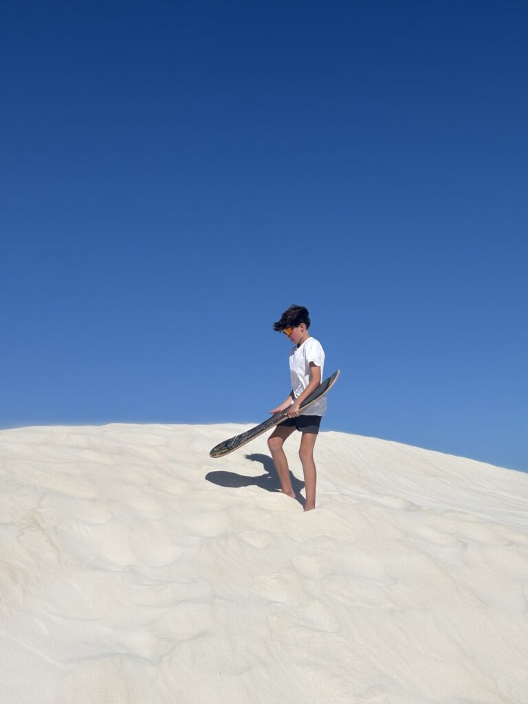 Célian fait du snowboard sur une dune de sable blanc.