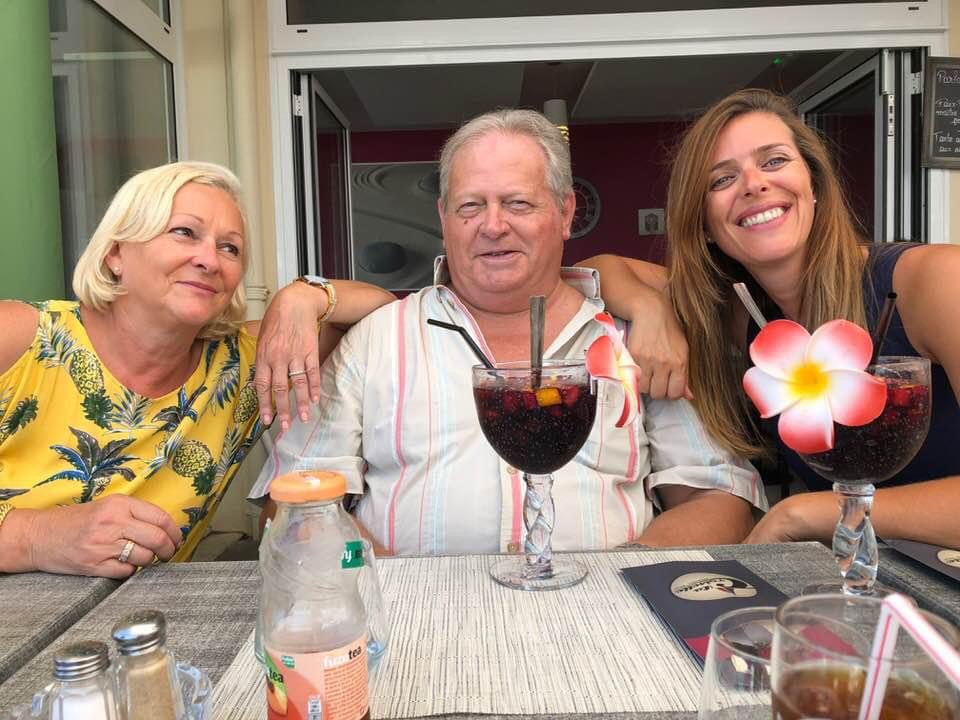 Photo de famille autour d’une table, avec un homme et deux femmes souriantes partageant un moment de complicité.