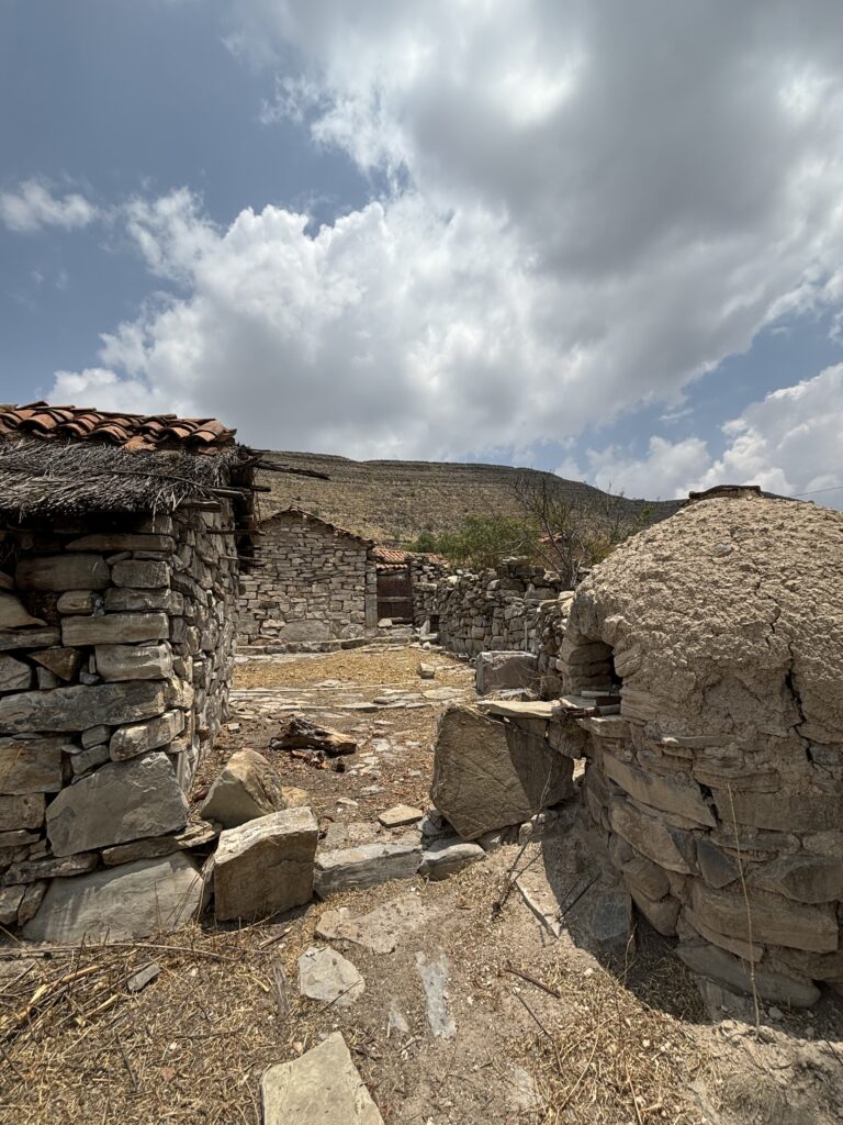 Vieilles habitations en pierre et toit de chaume dans un village andin de Bolivie, sous un ciel nuageux.
