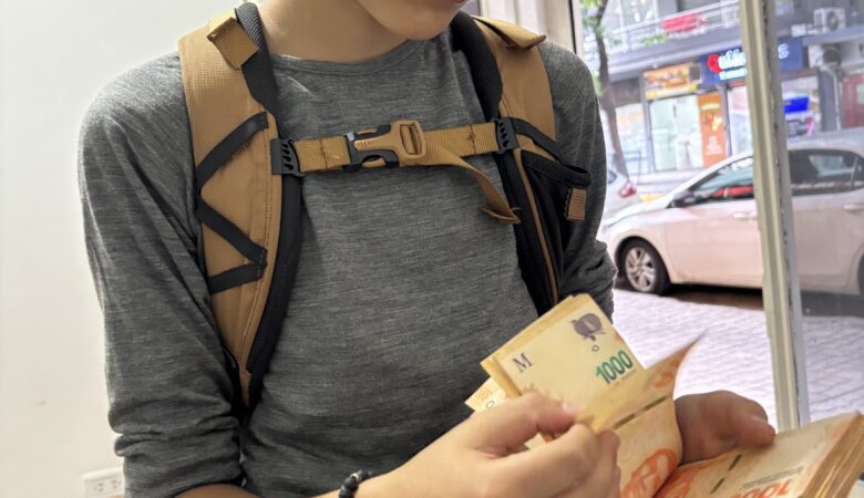 Jeune voyageur comptant des billets de pesos argentins à Buenos Aires, illustrant la dévaluation de la monnaie et les retraits en grosses coupures.